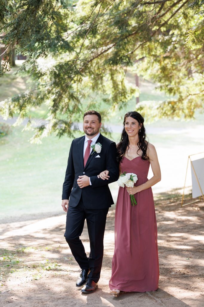 Bianca and Nick, the Lakewoods Resort wedding couple, walk hand-in-hand beneath tree branches, captured