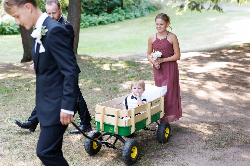 A young flower girl in a burgundy dress and a groomsmann in a suit walk
