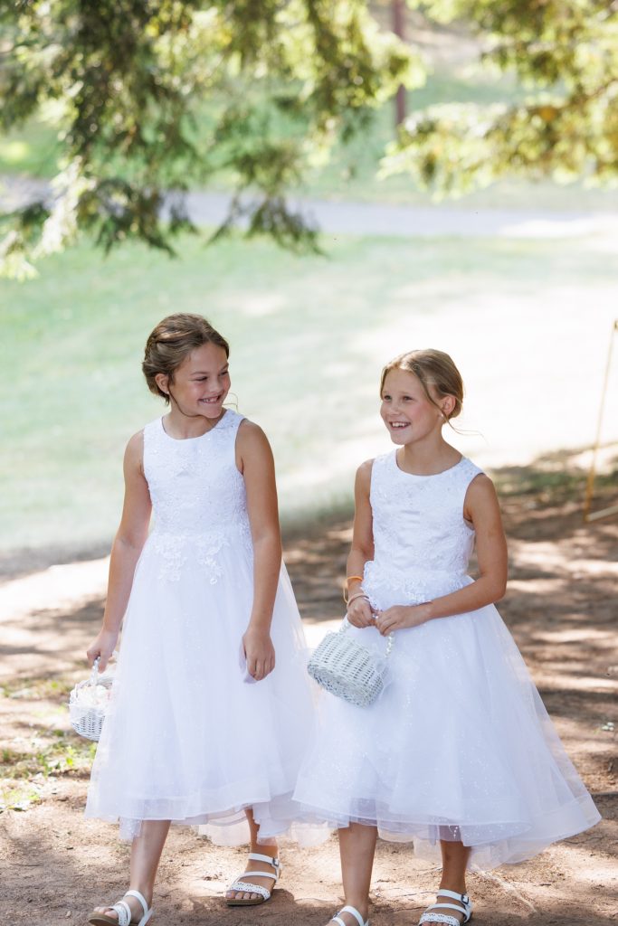 Two young flower girls in white dresses smiling and walking at a Lakewoods Resort wedding