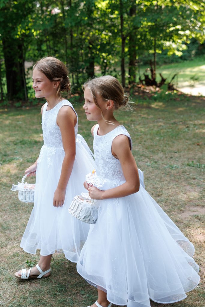 Two young flower girls in white lace dresses and sandals walking together at a Lakewoods