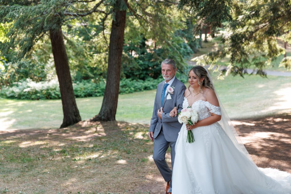 Bride in a flowing wedding gown and her father walking her down a grassy aisle