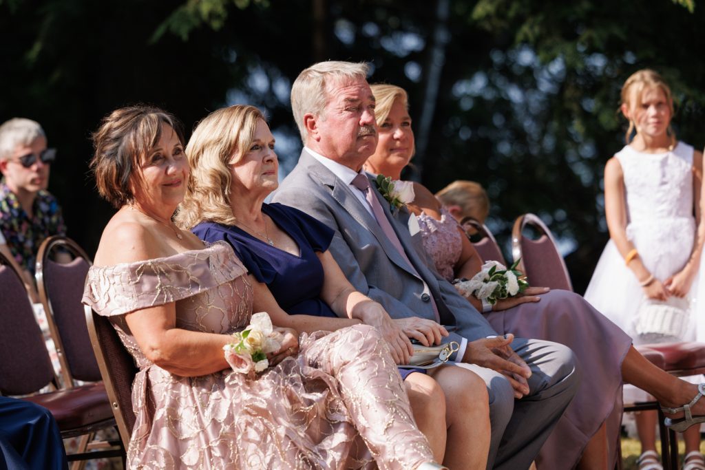 Wedding guests, including parents and a flower girl, attentively watch the ceremony at Lakewoods Resort