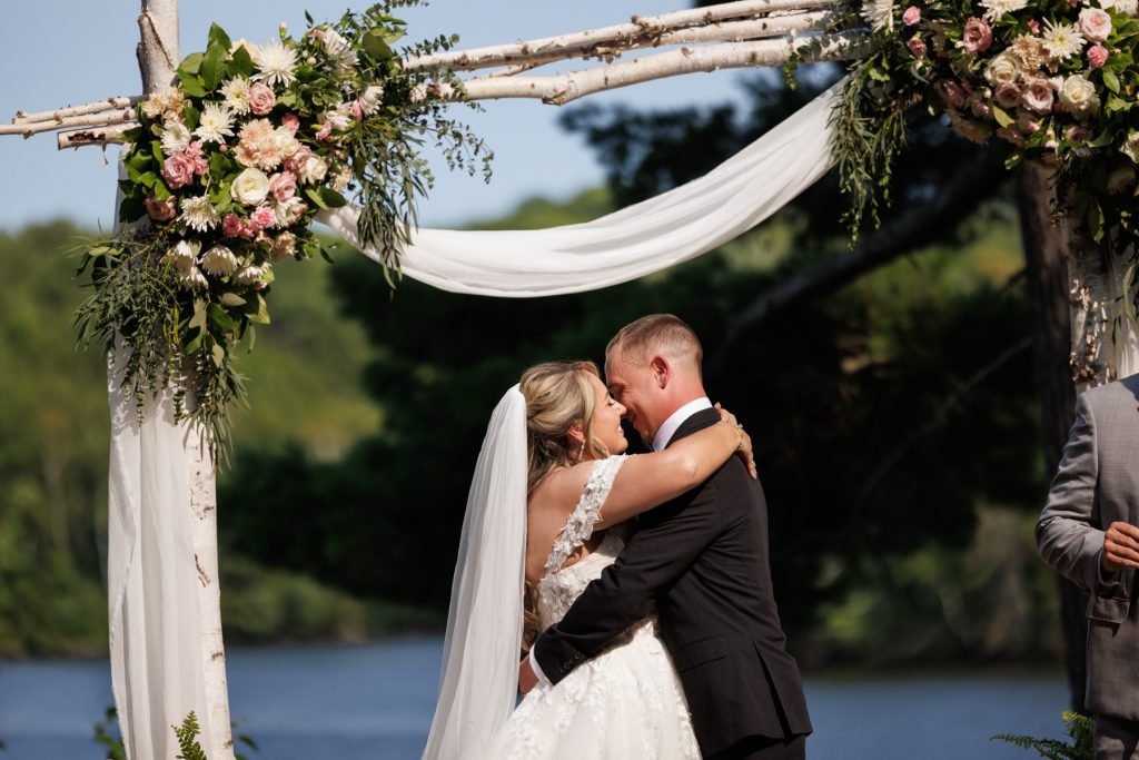 Bride and groom share a kiss under a floral birch arch at a Lakewoods Resort