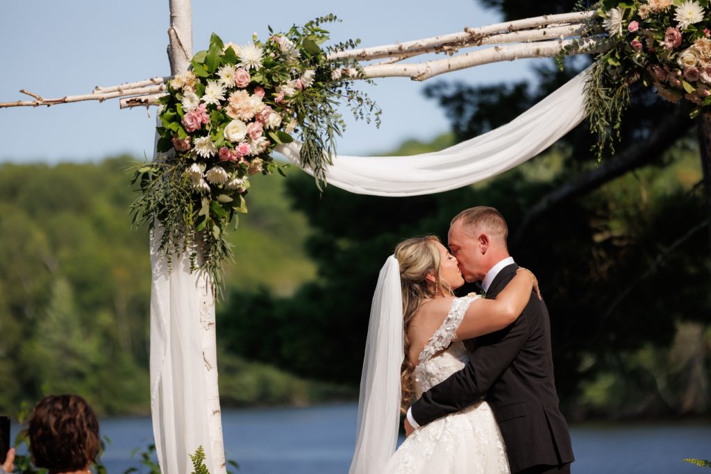 Bride and groom share a kiss beneath a floral-draped archway at a Lakewoods Resort wedding