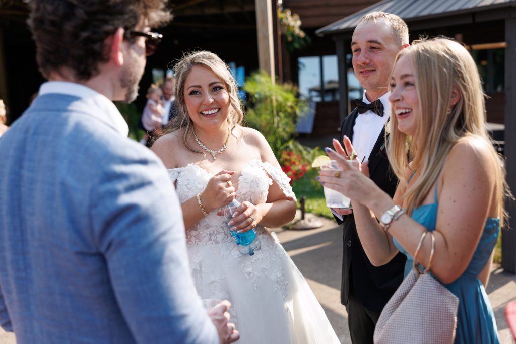 Bride in a lace wedding gown and groom laughing with guests at a Lakewoods Resort