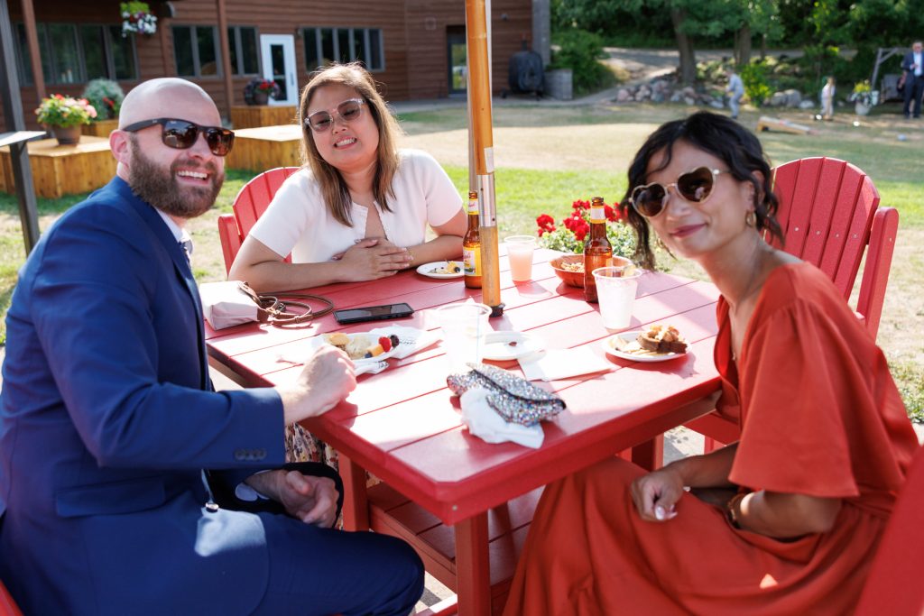 Three wedding guests, including a man in a suit, smiling and enjoying drinks and appetizers