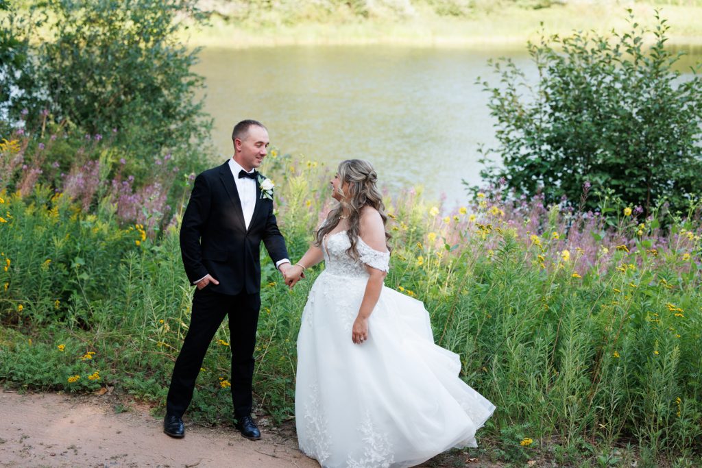 Bianca and Nick, the newly married couple, hold hands and smile near Lake Namekagon