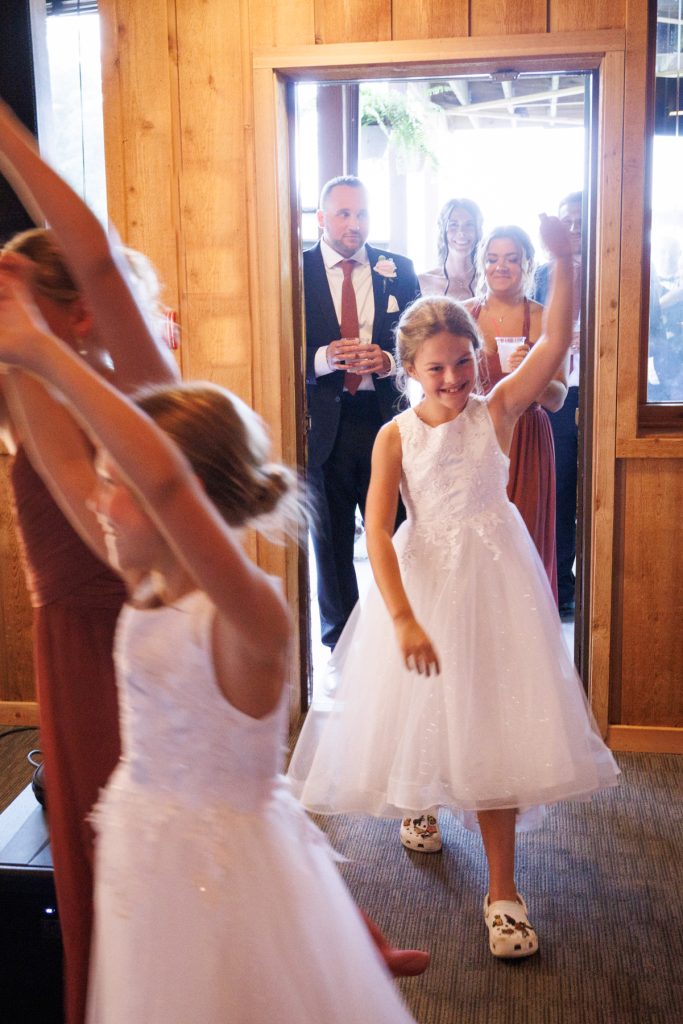 Young flower girls joyfully walking into a wedding reception at Lakewoods Resort, captured by Beau