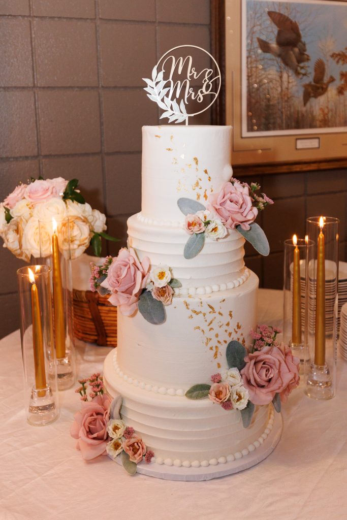 Elegant three-tiered wedding cake with floral decorations and gold accents, showcased at a Lakewoods Resort