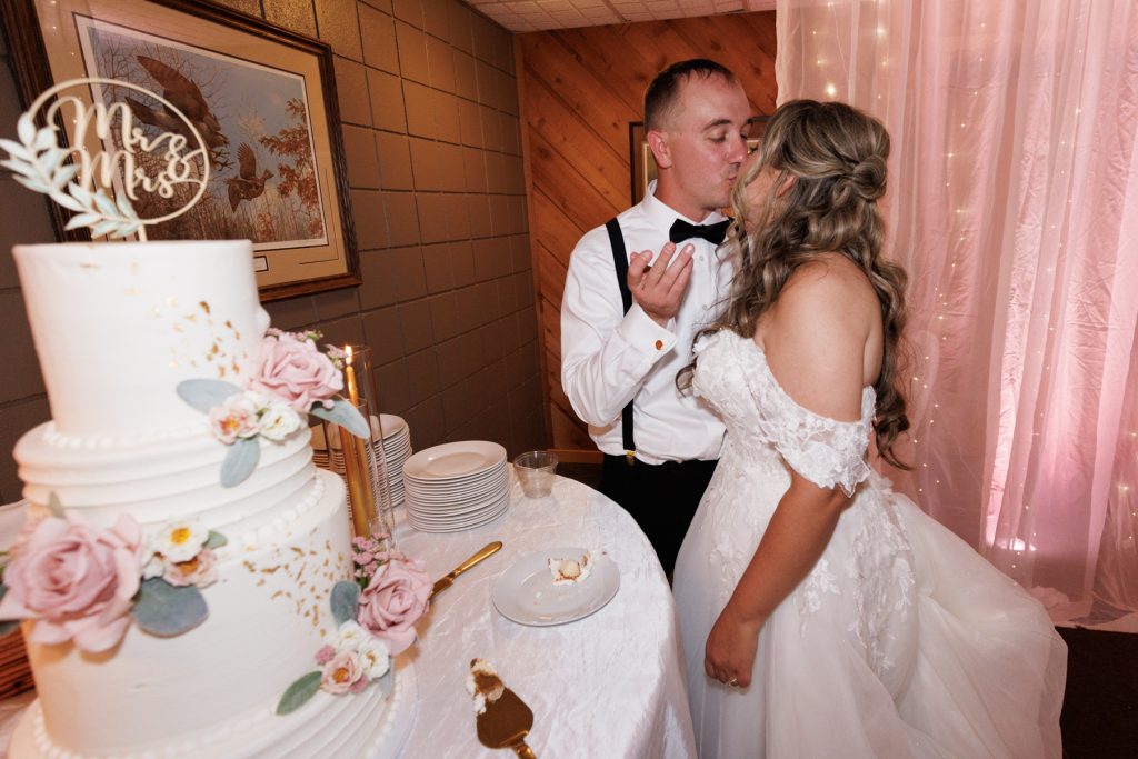 Bride and groom kissing in front of a multi-tiered wedding cake at Lakewoods Resort