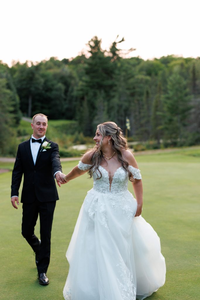 Bianca and Nick, the happy couple, walk hand-in-hand on the green lawn at Lakewoods Resort