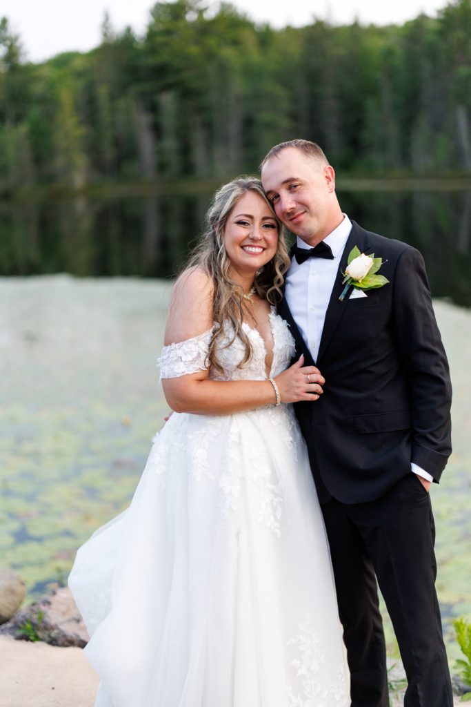 Bianca and Nick, the happy couple, embrace in formal wedding attire with Lake Namekagon visible