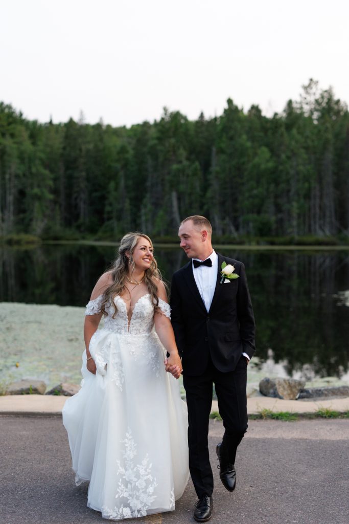 Bianca and Nick, the newlyweds, hold hands and smile while walking together at Lakewoods Resort