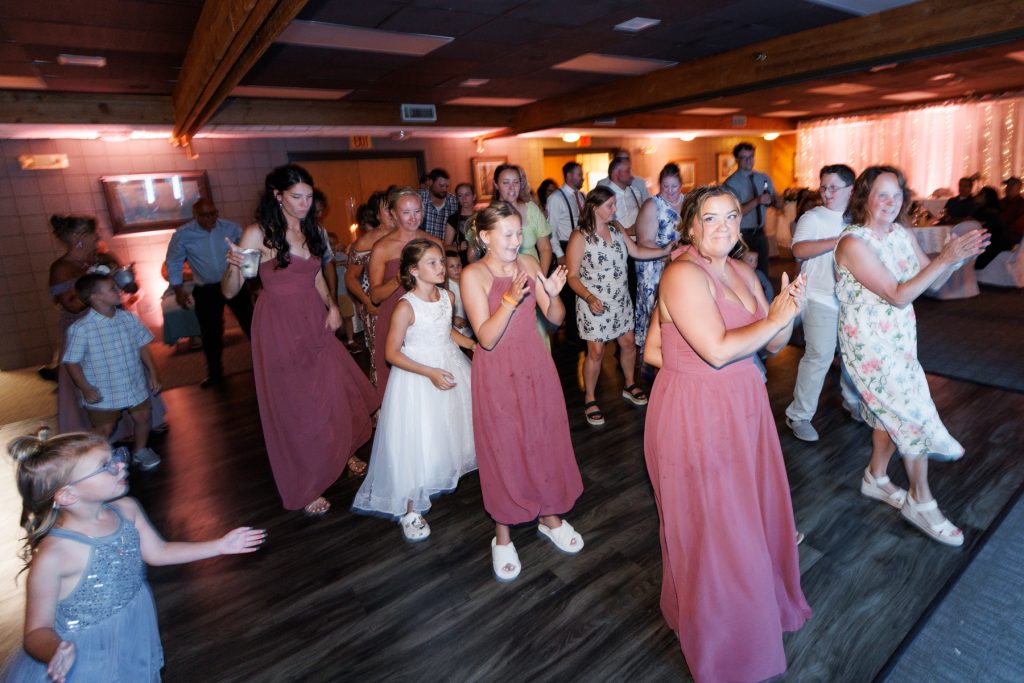 Group of wedding guests, including bridesmaids and flower girls, joyfully clapping and dancing