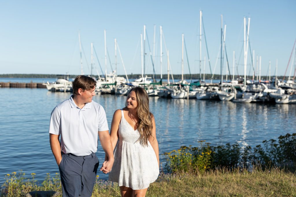 Cassie and Daniel, an engaged couple, hold hands smiling at each other with a backdrop