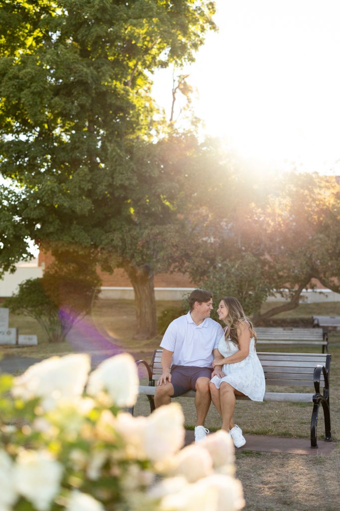 Cassie and Daniel, the engaged couple, sit closely on a park bench during their Lake
